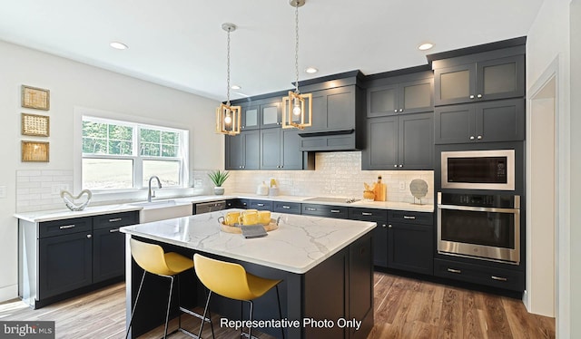 kitchen with a center island, appliances with stainless steel finishes, decorative light fixtures, light stone counters, and wood-type flooring