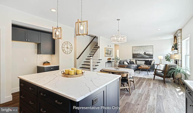 kitchen with tasteful backsplash, light stone counters, pendant lighting, hardwood / wood-style floors, and a kitchen island