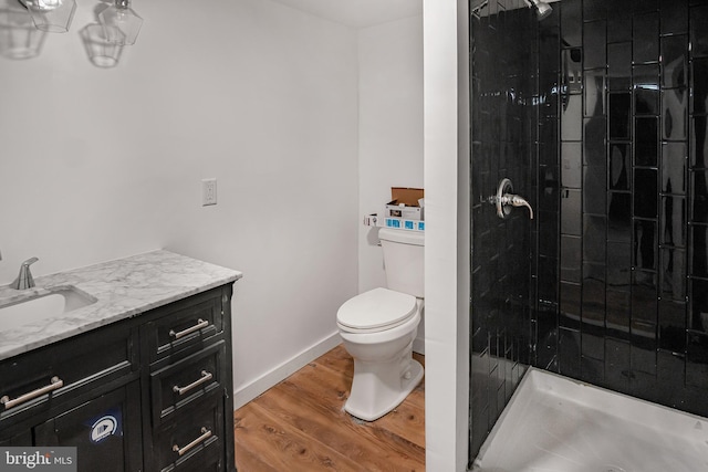 bathroom featuring a tile shower, vanity, hardwood / wood-style flooring, and toilet