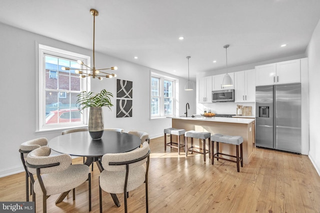 dining area with an inviting chandelier, sink, and light hardwood / wood-style flooring