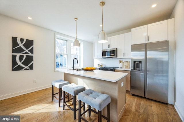 kitchen featuring appliances with stainless steel finishes, a breakfast bar, a center island with sink, white cabinets, and hanging light fixtures