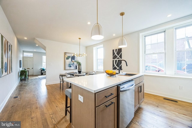 kitchen featuring dishwasher, a center island with sink, sink, light wood-type flooring, and decorative light fixtures