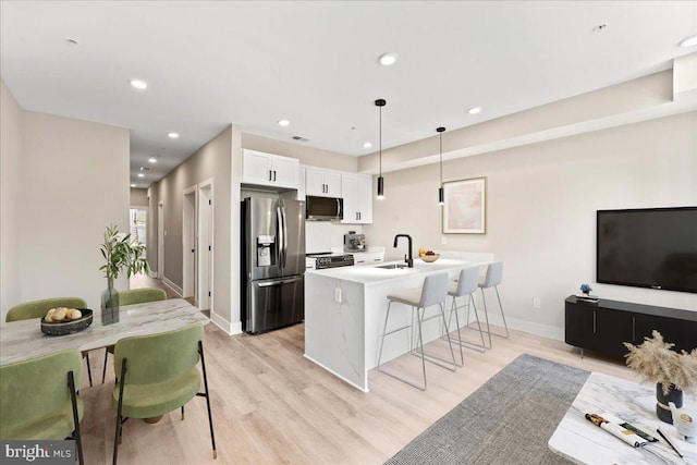 kitchen featuring sink, white cabinetry, stainless steel appliances, an island with sink, and decorative light fixtures