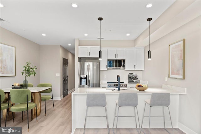 kitchen featuring hanging light fixtures, stainless steel appliances, white cabinets, and a kitchen bar