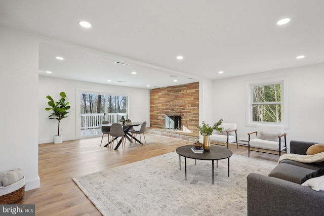 living room with light wood-type flooring, a large fireplace, and a healthy amount of sunlight