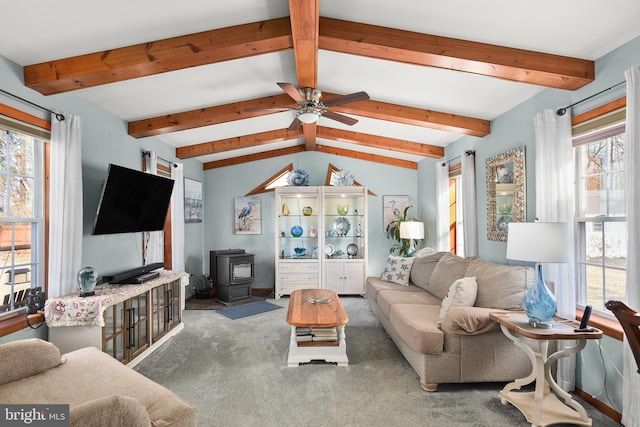 carpeted living room featuring lofted ceiling with beams, ceiling fan, plenty of natural light, and a wood stove