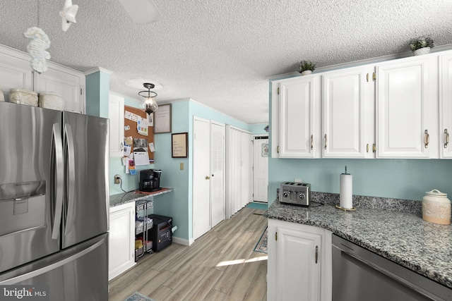 kitchen with white cabinets, dark stone countertops, light wood-type flooring, appliances with stainless steel finishes, and decorative light fixtures