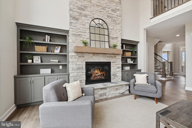 living room featuring a towering ceiling, a fireplace, built in features, and light hardwood / wood-style flooring