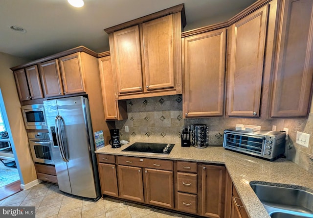 kitchen featuring tasteful backsplash, sink, light stone countertops, appliances with stainless steel finishes, and light tile patterned floors