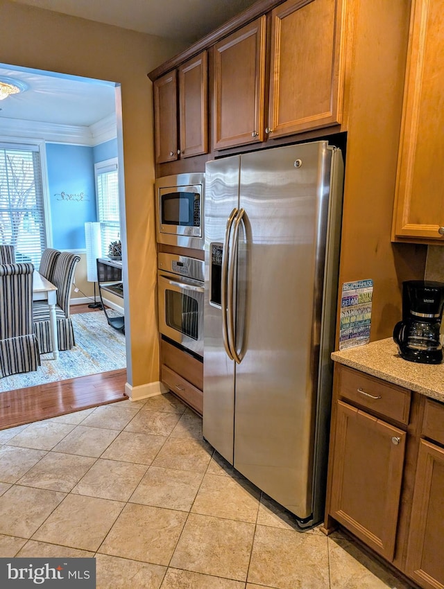 kitchen featuring light stone counters, appliances with stainless steel finishes, ornamental molding, and light tile patterned flooring