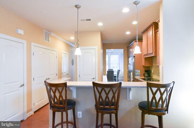 kitchen with pendant lighting, a kitchen bar, black electric stovetop, stainless steel fridge, and light stone counters