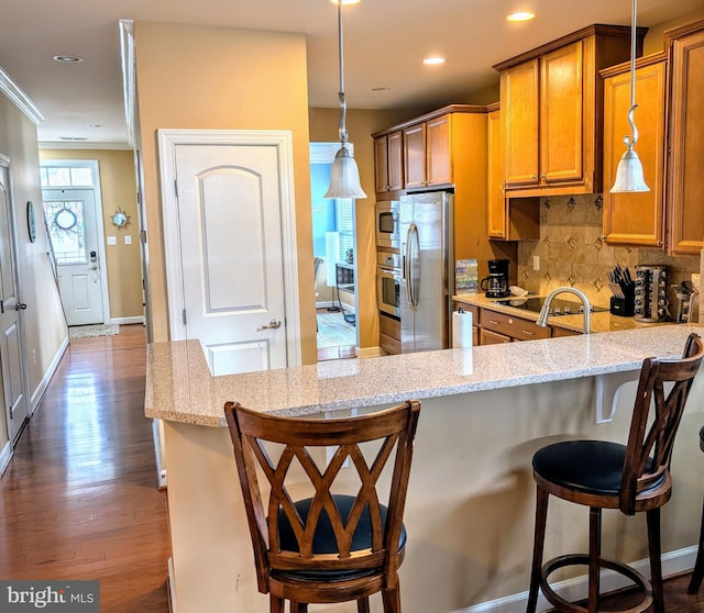 kitchen with hanging light fixtures, appliances with stainless steel finishes, kitchen peninsula, and a breakfast bar