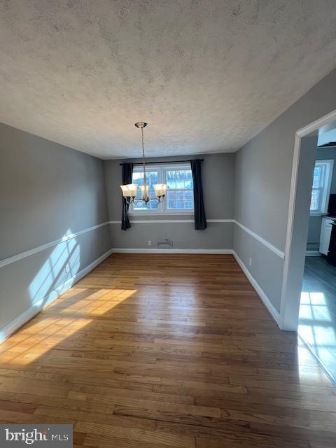 unfurnished dining area with a textured ceiling, dark hardwood / wood-style floors, and an inviting chandelier