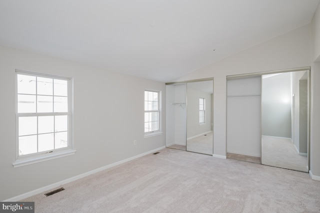 unfurnished bedroom with multiple closets, vaulted ceiling, and light carpet