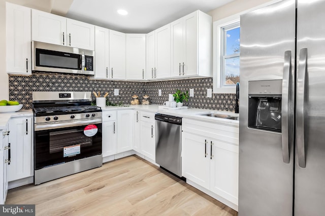 kitchen featuring tasteful backsplash, stainless steel appliances, white cabinets, and light wood-type flooring