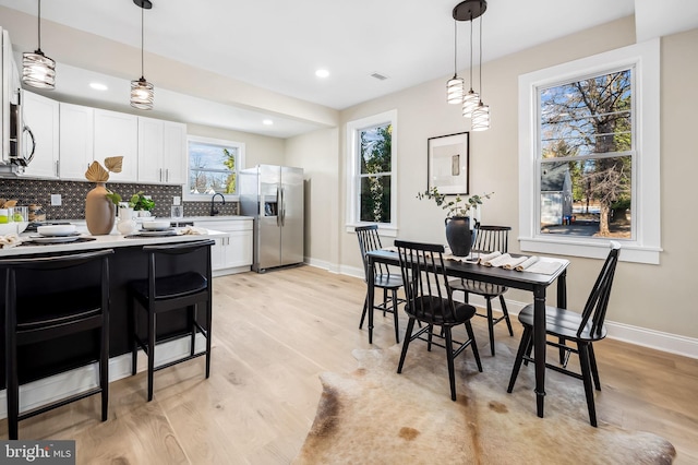 kitchen with pendant lighting, tasteful backsplash, white cabinets, stainless steel fridge with ice dispenser, and light wood-type flooring