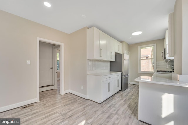 kitchen with white cabinets, appliances with stainless steel finishes, decorative backsplash, and light hardwood / wood-style flooring