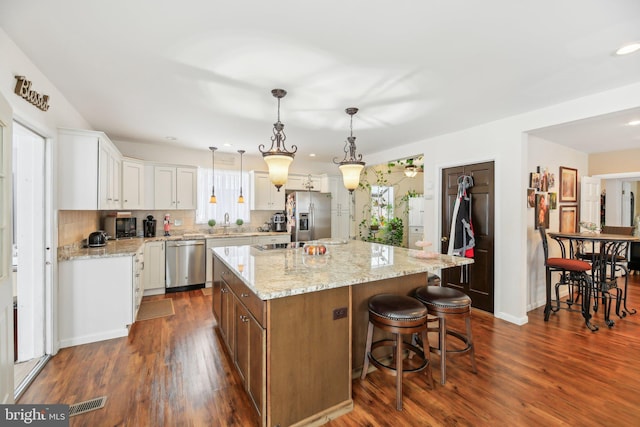 kitchen with appliances with stainless steel finishes, backsplash, decorative light fixtures, white cabinets, and a kitchen island