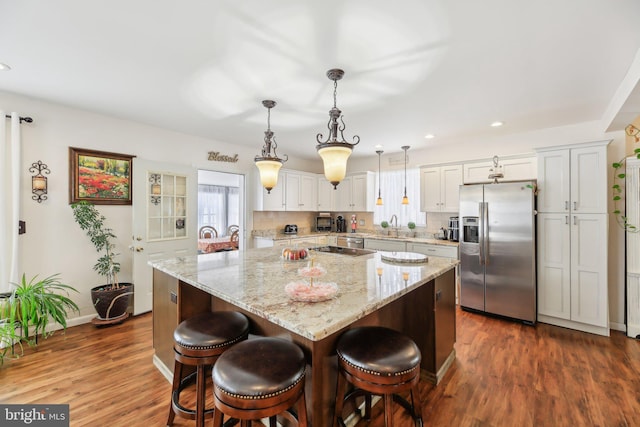 kitchen with appliances with stainless steel finishes, white cabinets, a kitchen island, hanging light fixtures, and a breakfast bar area