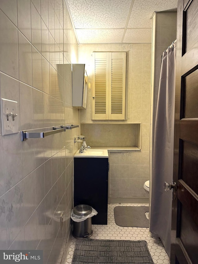 bathroom featuring tile patterned floors, vanity, a drop ceiling, and tile walls