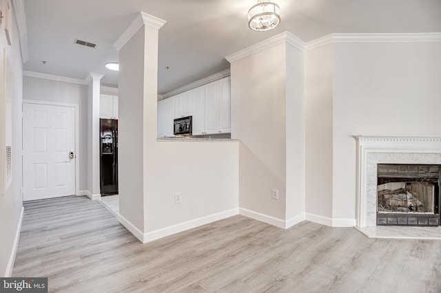 unfurnished living room with light wood-type flooring, visible vents, a fireplace, crown molding, and baseboards