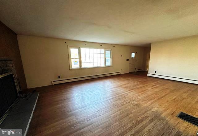 unfurnished living room with a stone fireplace, wood-type flooring, and a baseboard heating unit