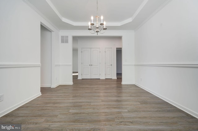 unfurnished dining area with visible vents, a tray ceiling, wood finished floors, baseboards, and a chandelier