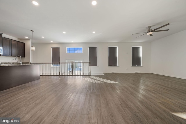 unfurnished living room featuring recessed lighting, baseboards, dark wood-style floors, and a sink