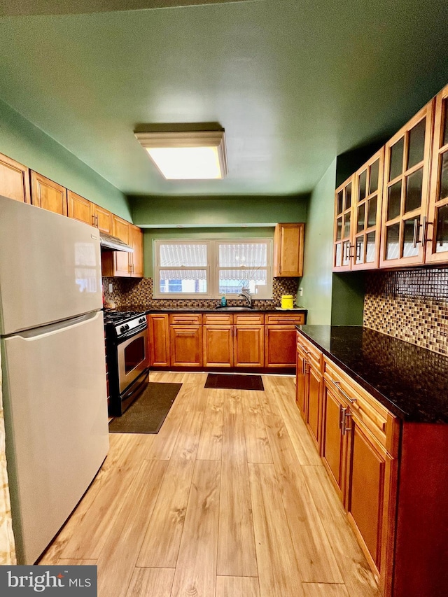 kitchen featuring white refrigerator, tasteful backsplash, light hardwood / wood-style flooring, and range with gas cooktop