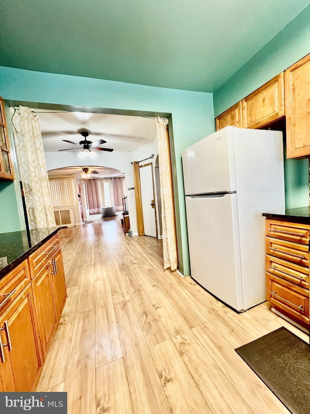 kitchen featuring dark stone countertops, ceiling fan, light hardwood / wood-style flooring, and white fridge