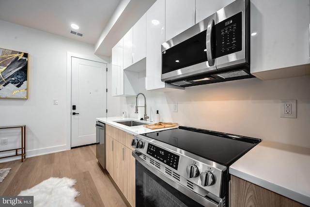 kitchen with appliances with stainless steel finishes, light hardwood / wood-style floors, white cabinetry, and sink