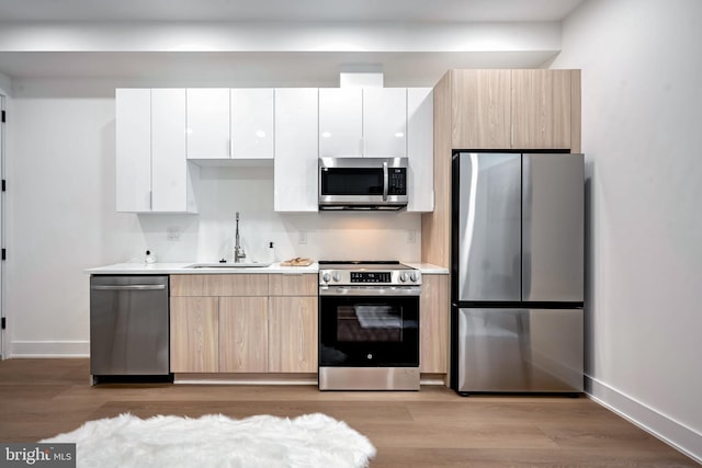 kitchen with light brown cabinets, white cabinets, sink, appliances with stainless steel finishes, and light hardwood / wood-style floors