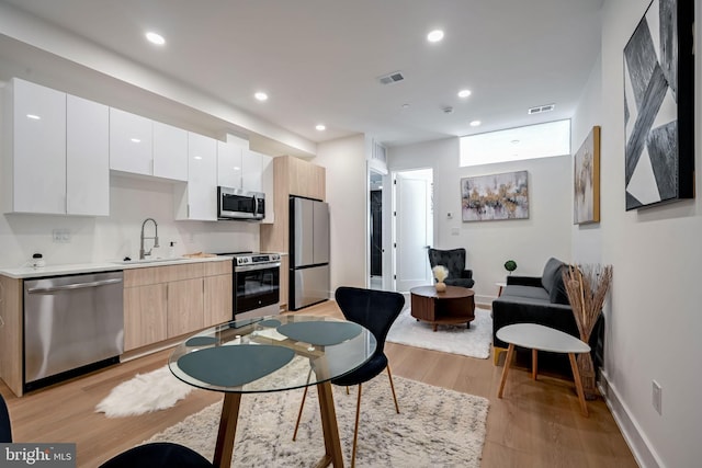 kitchen featuring light brown cabinetry, stainless steel appliances, sink, light hardwood / wood-style floors, and white cabinetry