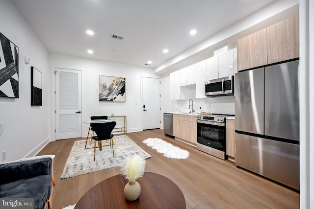 kitchen with white cabinets, sink, light brown cabinetry, light hardwood / wood-style floors, and stainless steel appliances