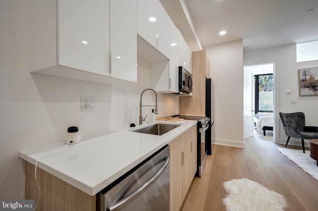 kitchen featuring white cabinetry, sink, stainless steel appliances, and light wood-type flooring