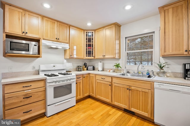 kitchen with light brown cabinets, light wood-type flooring, sink, and white appliances