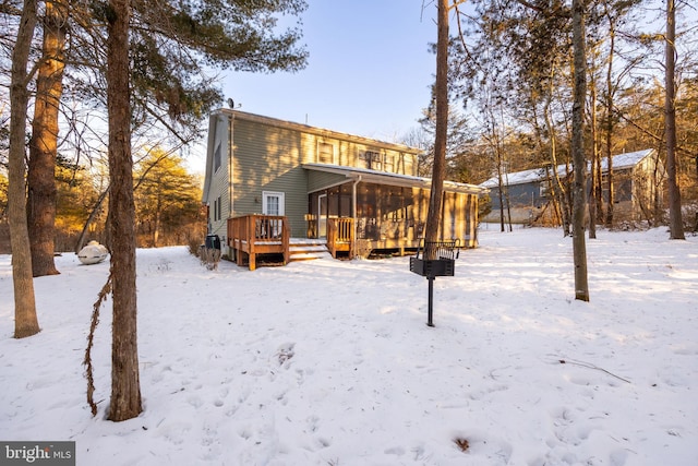 snow covered rear of property with a wooden deck and a sunroom