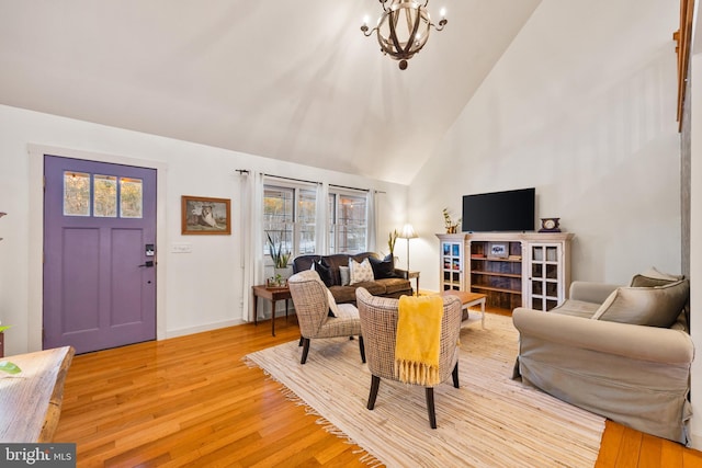 living room with high vaulted ceiling, an inviting chandelier, and light hardwood / wood-style floors