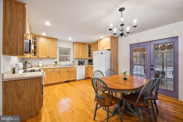 dining room with sink, light wood-type flooring, french doors, and an inviting chandelier