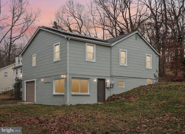 back house at dusk featuring a yard and a garage