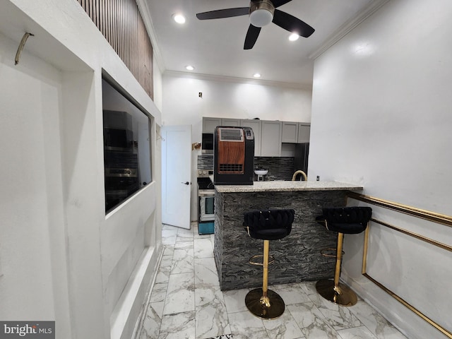 kitchen featuring tasteful backsplash, ceiling fan, crown molding, gray cabinets, and a breakfast bar area