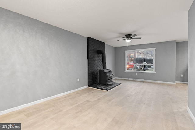 unfurnished living room featuring a wood stove, ceiling fan, and light hardwood / wood-style floors