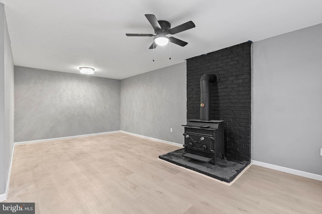 unfurnished living room with ceiling fan, light hardwood / wood-style floors, and a wood stove