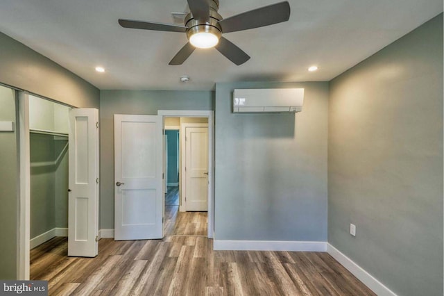 unfurnished bedroom with hardwood / wood-style floors, a closet, a wall mounted AC, and ceiling fan