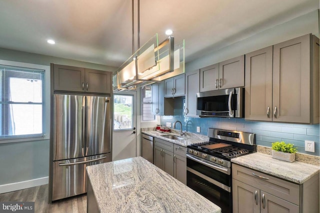 kitchen featuring sink, light stone counters, pendant lighting, decorative backsplash, and appliances with stainless steel finishes