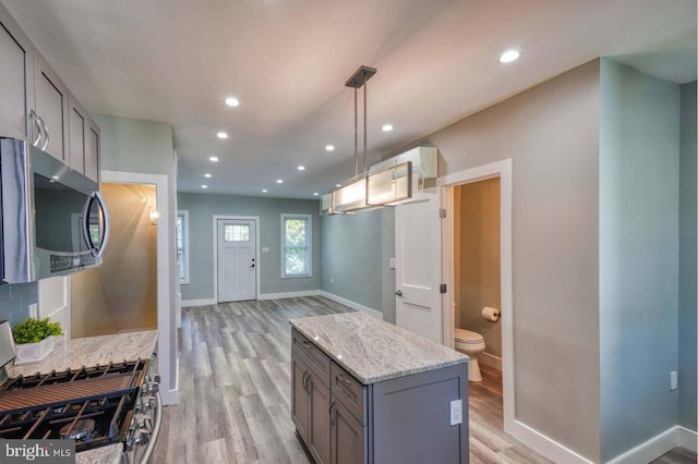 kitchen featuring gray cabinetry, light stone counters, light hardwood / wood-style floors, pendant lighting, and appliances with stainless steel finishes