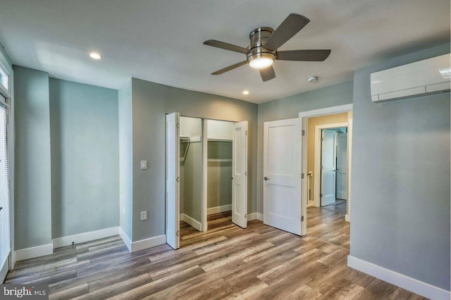 unfurnished bedroom with a wall mounted air conditioner, ceiling fan, and hardwood / wood-style floors