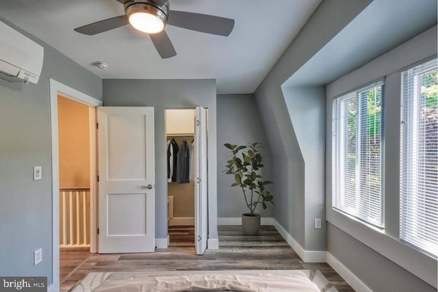 unfurnished bedroom with a wall unit AC, ceiling fan, wood-type flooring, a spacious closet, and a closet