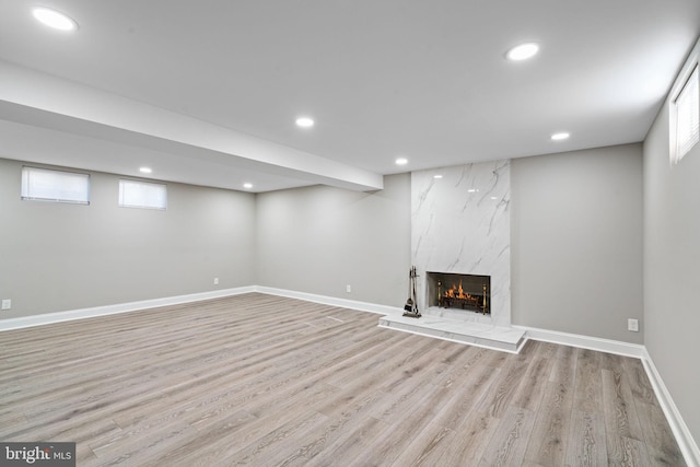 basement featuring a wealth of natural light, a high end fireplace, and light wood-type flooring