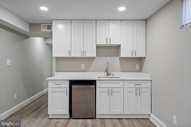 kitchen featuring white cabinetry, sink, stainless steel dishwasher, and light hardwood / wood-style flooring